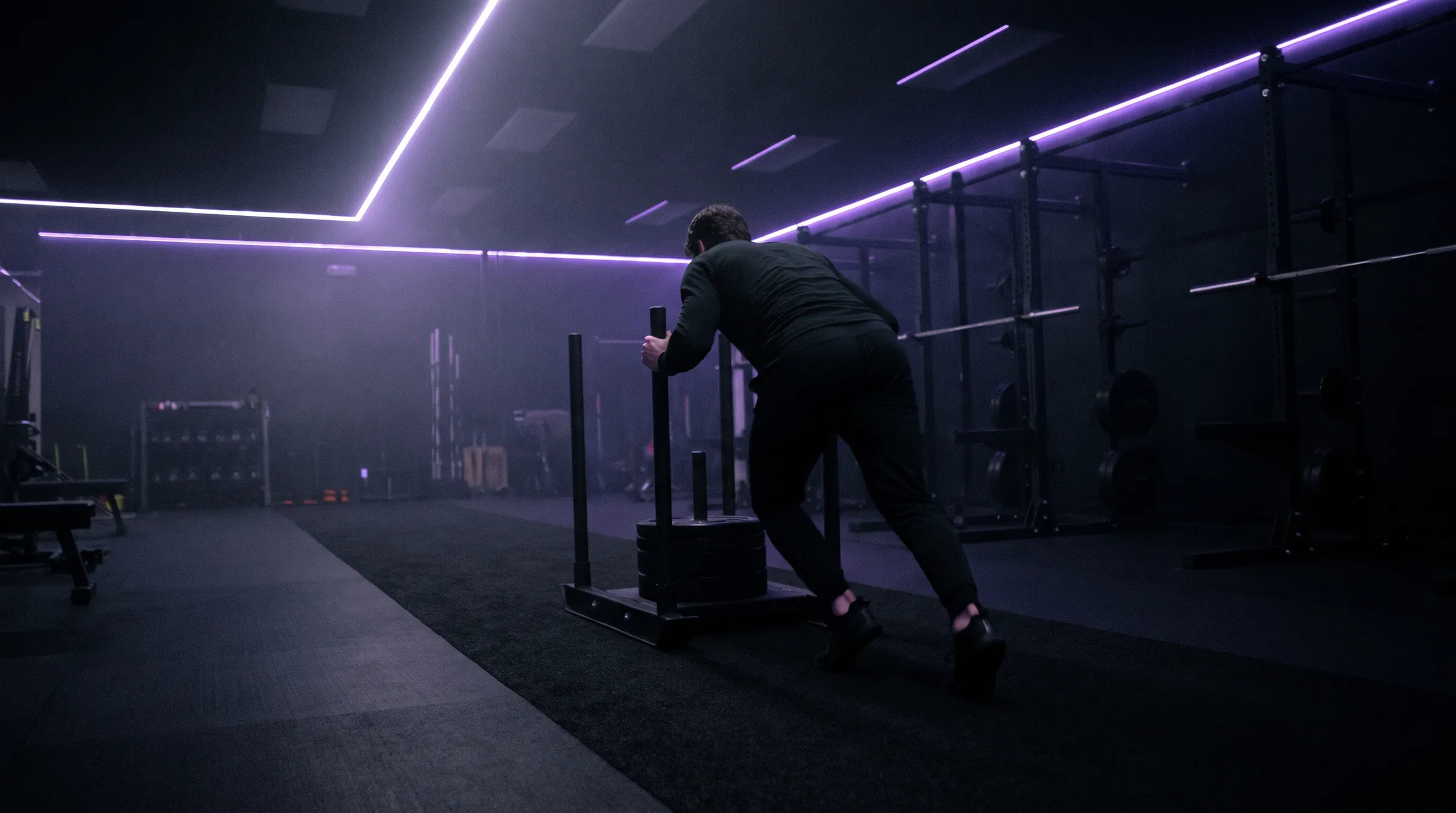 Dark training lab with violet light strips and an athlete pushing a sled